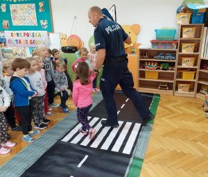 Policjant pokazujący dzieciom jak bezpiecznie przechodzić przez pasy na macie edukacyjnej